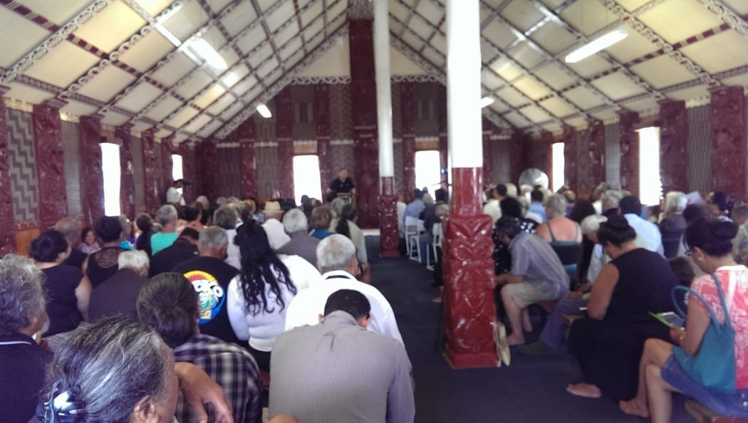 A gathering of people seated inside a carved wharenui